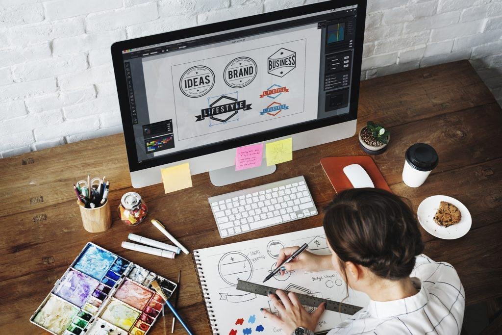 Diseñador gráfico bocetando y enfrente de su computadora con logos